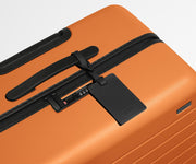 The Medium suitcase in Sorbet Orange shown shown from above highlighting TSA-approved combination lock and recycled leather luggage tag