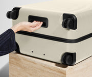 White suitcase with black handles and wheels on a light wooden surface.