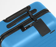 The Bigger Carry-On suitcase in Splash Blue shown shown from above highlighting TSA-approved combination lock and recycled leather luggage tag