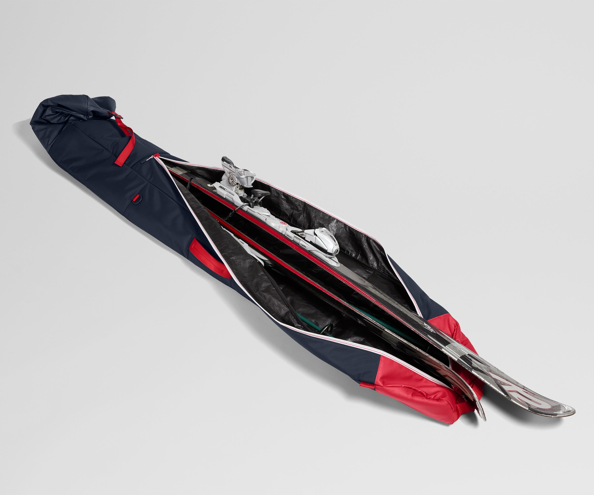 Pair of skis in a navy and red carrying case on a light gray background