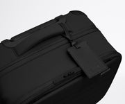 The Softside Compact Carry-On suitcase in Jet Black shown shown from above highlighting the recycled leather luggage tag