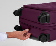 The Softside Carry-On suitcase in Plum Purple shown laying on a surface to highlight the underside grab handle