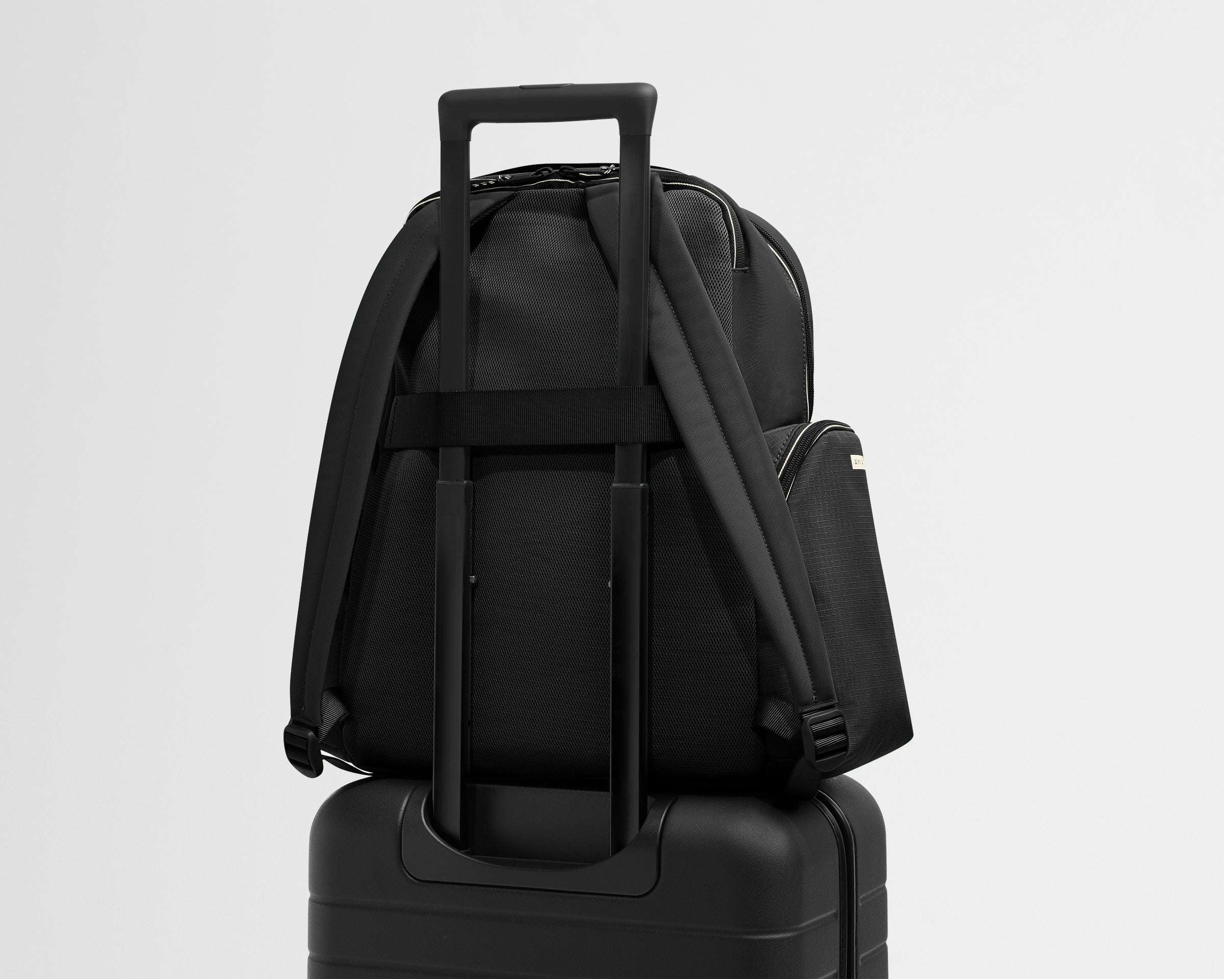 Black backpack on top of a black suitcase with a light gray background