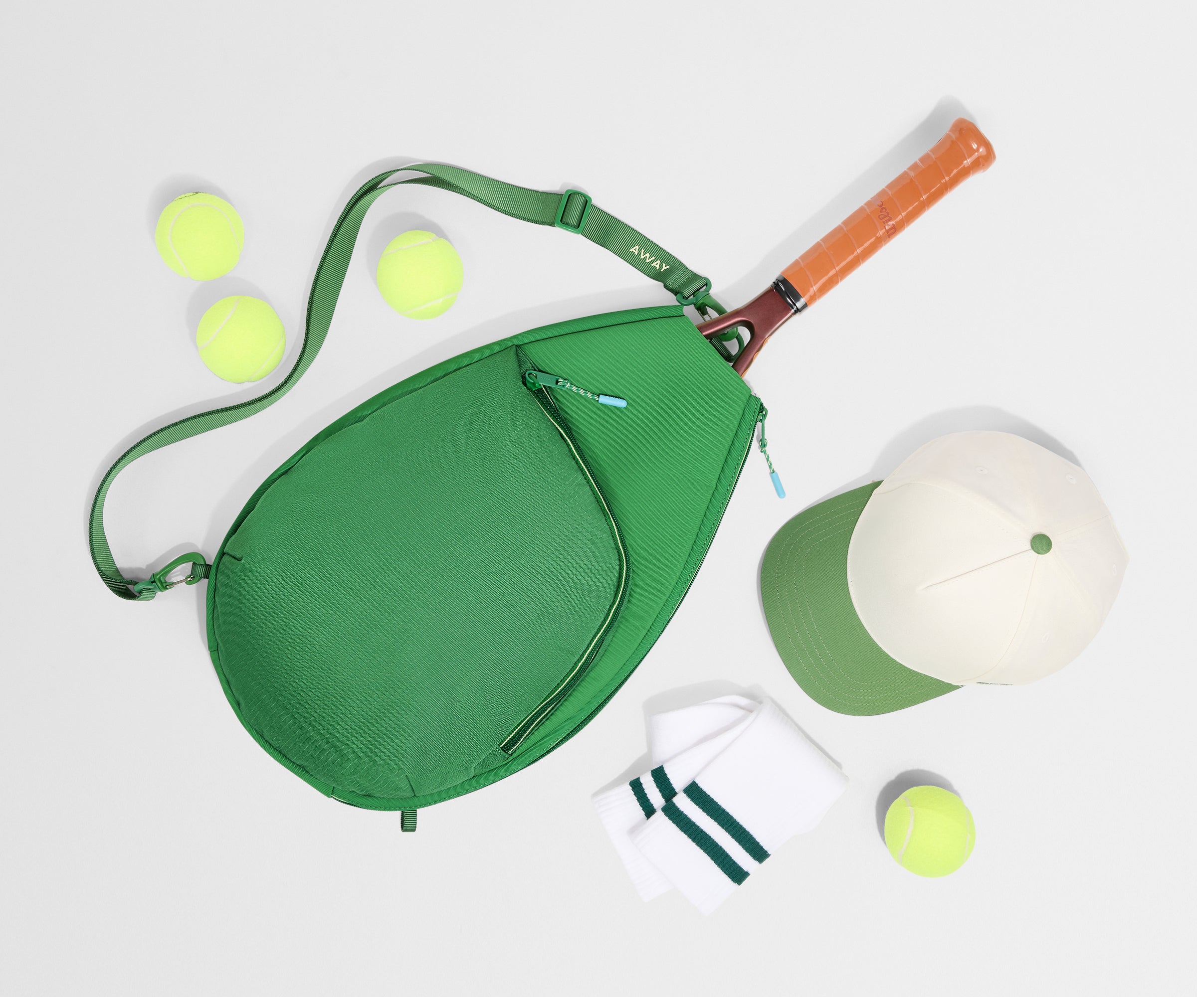 Green tennis bag with tennis racket, balls, and cap on a white background