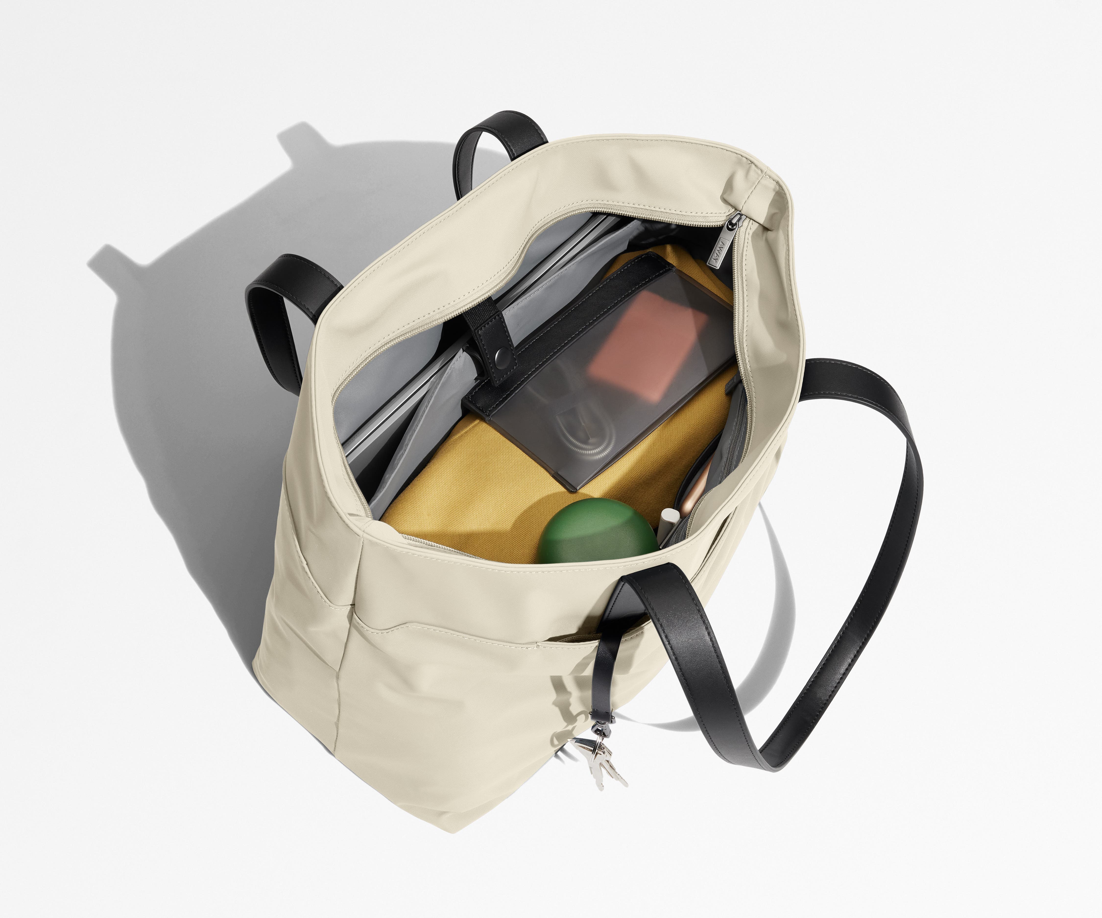 Tote bag packed with a laptop, water bottle, travel pouch, and sweater. A key is attached to the hidden key leash