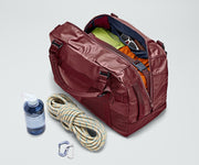 Active Duffle 55L packed with travel essentials and outdoor gear including a packing cube, sunglasses, wallet, carabiner and rope, and water bottle