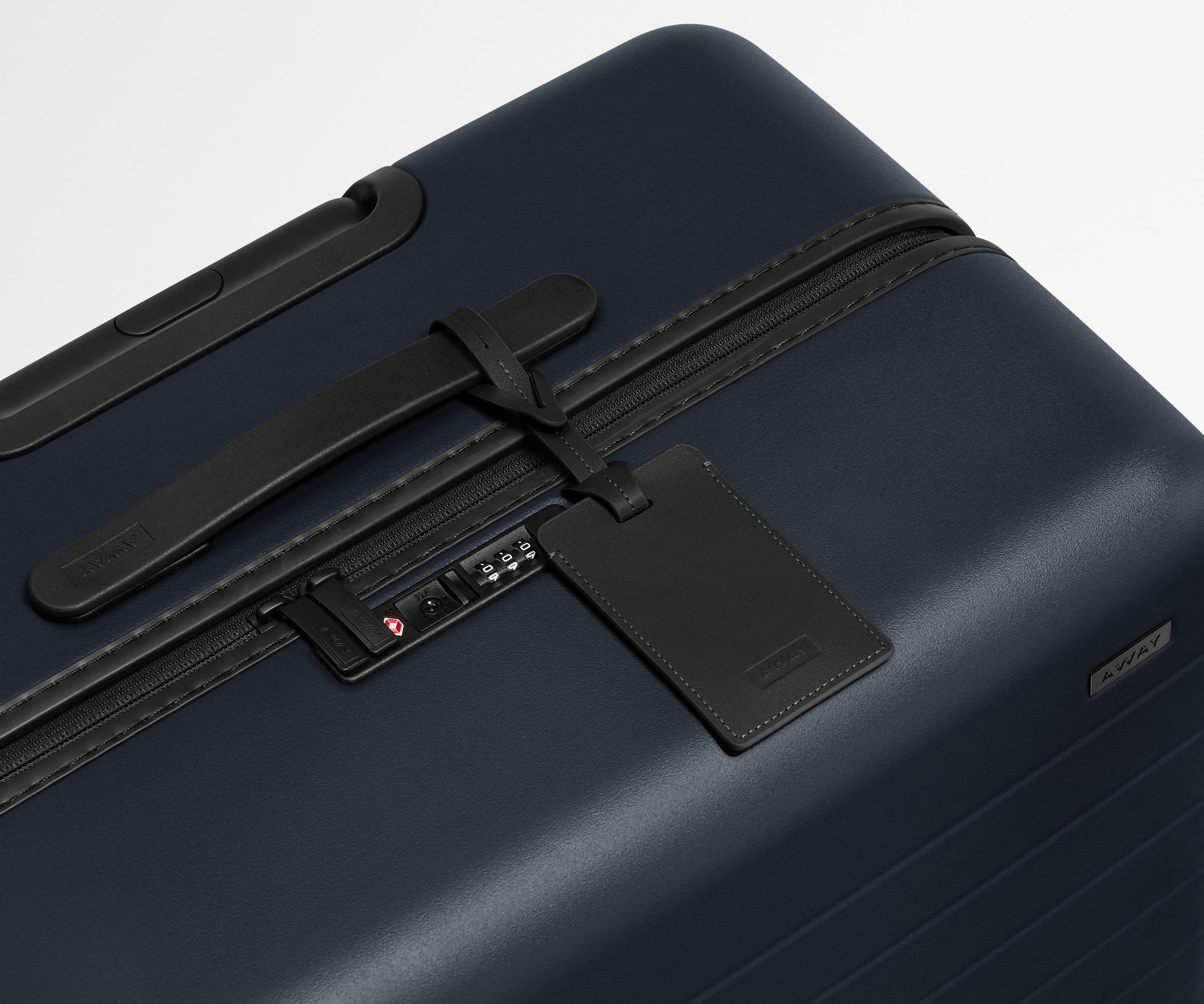The Medium suitcase in Navy Blue shown shown from above highlighting TSA-approved combination lock and recycled leather luggage tag