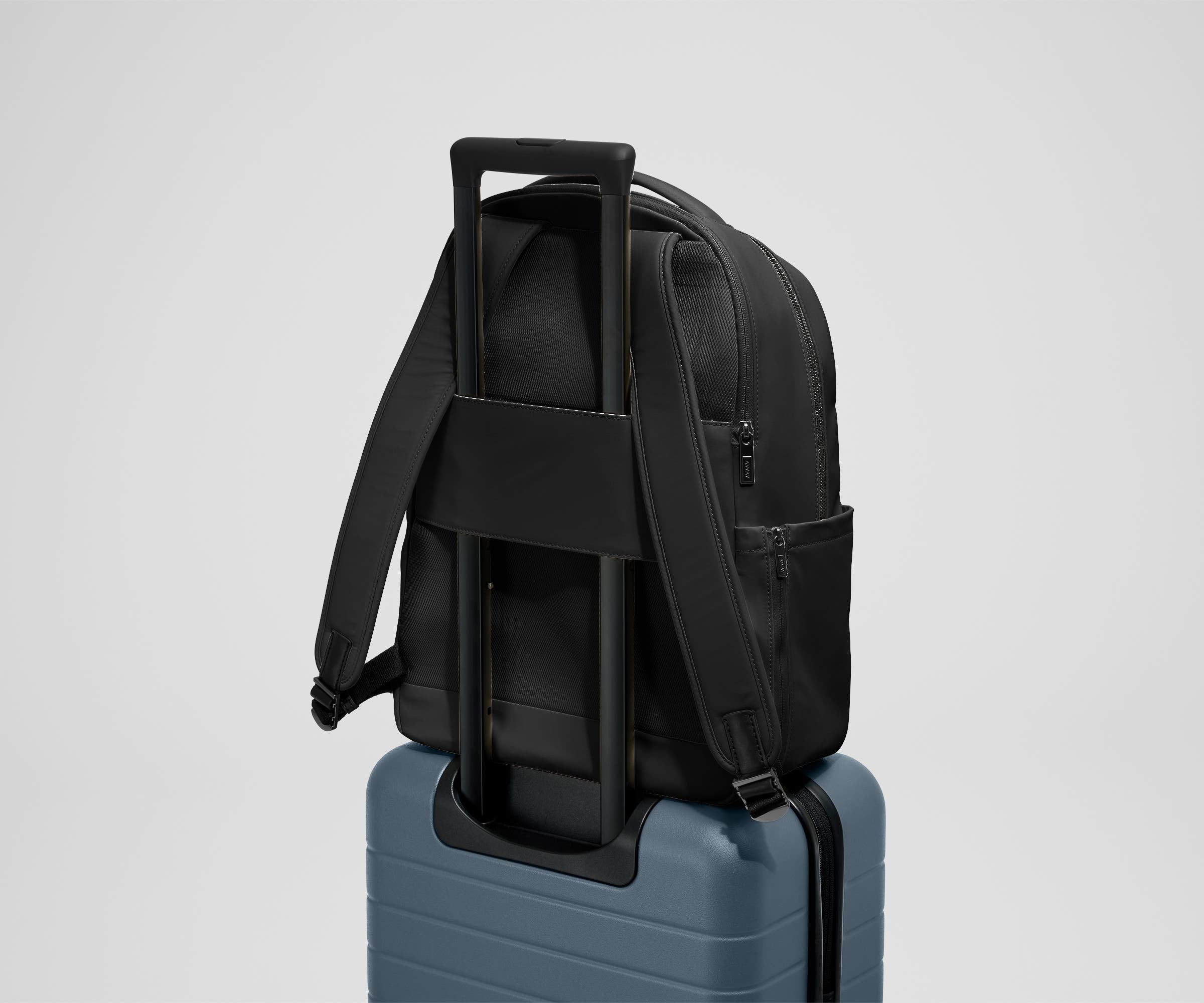 The Commuter Backpack on top of an Away suitcase, attached by the trolley pass-through sleeve