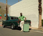 Influencer @danclemt posing against a retro green truck and California street backdrop with The Large suitcase in Sea Green