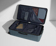 The Trunk suitcase in Coast Blue shown open on its side and packed with Away's packing organizers to show capacity and the interior compression system, designed to help you pack more in