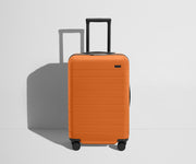 Front product view of The Bigger Carry-On Flex suitcase in Sorbet Orange with raised handle