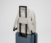 The Commuter Backpack on top of an Away suitcase, attached by the trolley pass-through sleeve
