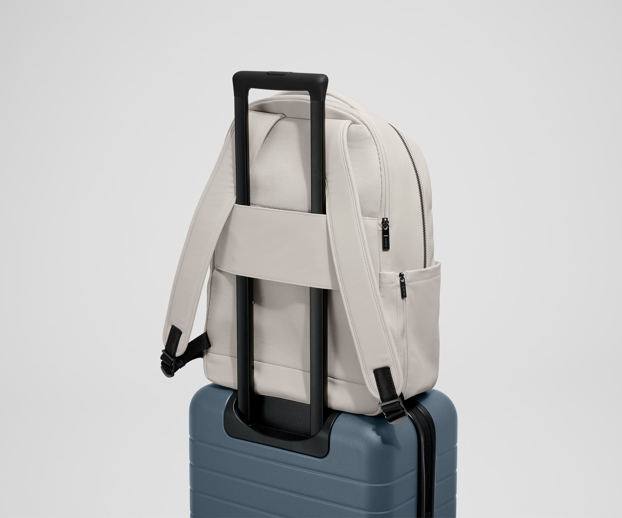 The Commuter Backpack on top of an Away suitcase, attached by the trolley pass-through sleeve