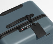 The Trunk suitcase in Coast Blue shown shown from above highlighting TSA-approved combination lock and recycled leather luggage tag