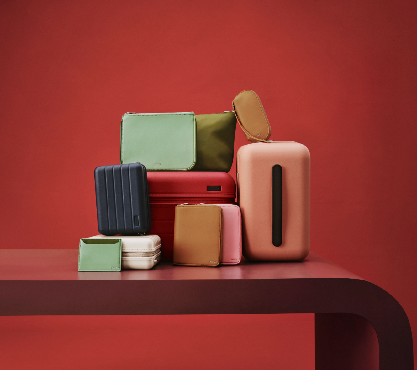 A group of Away accessories in various colors stacked on top of each other on a red background