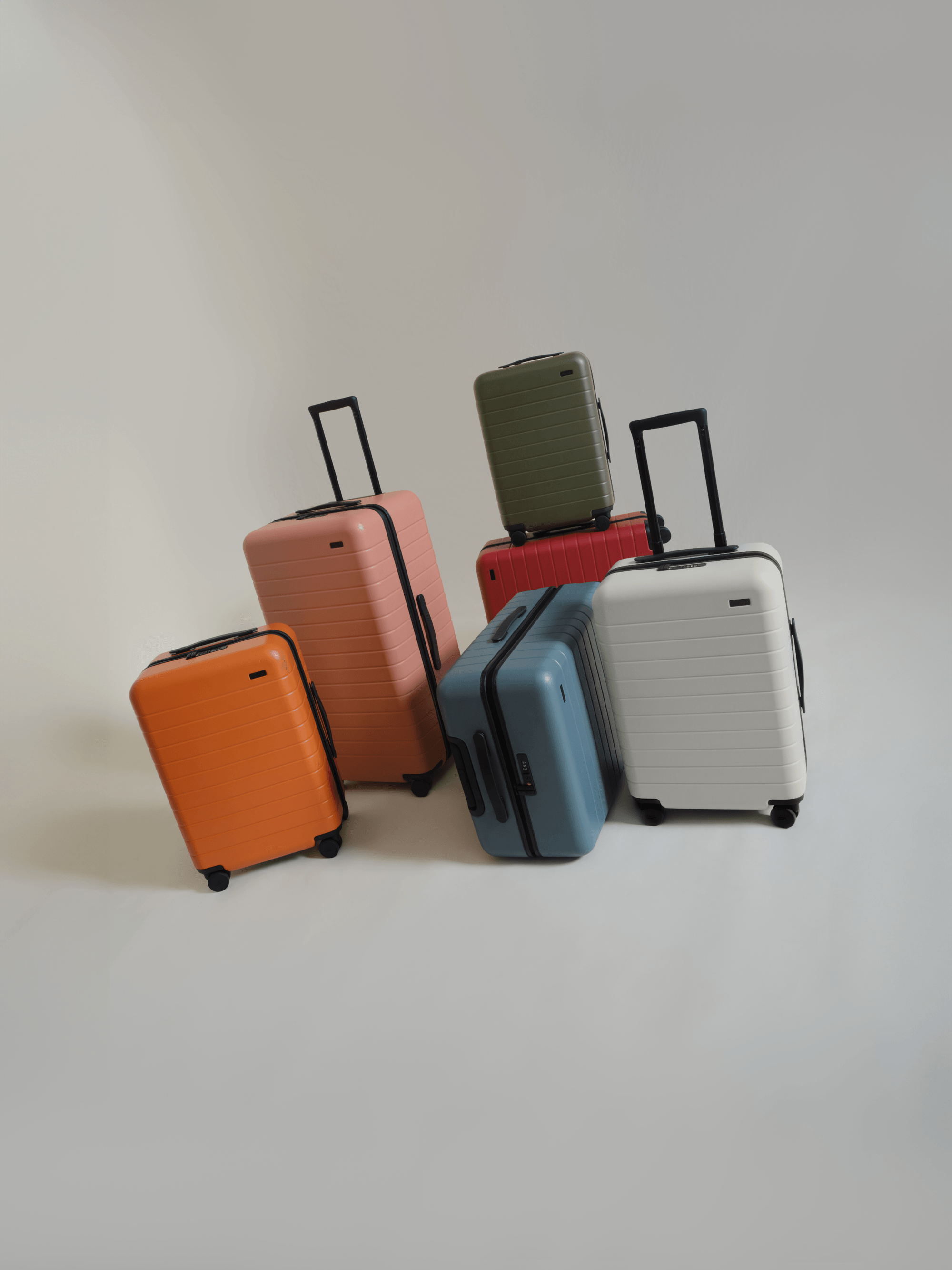 A collection of 6 Away suitcases in various sizes in orange, pink, blue, white, red, and green on a white background