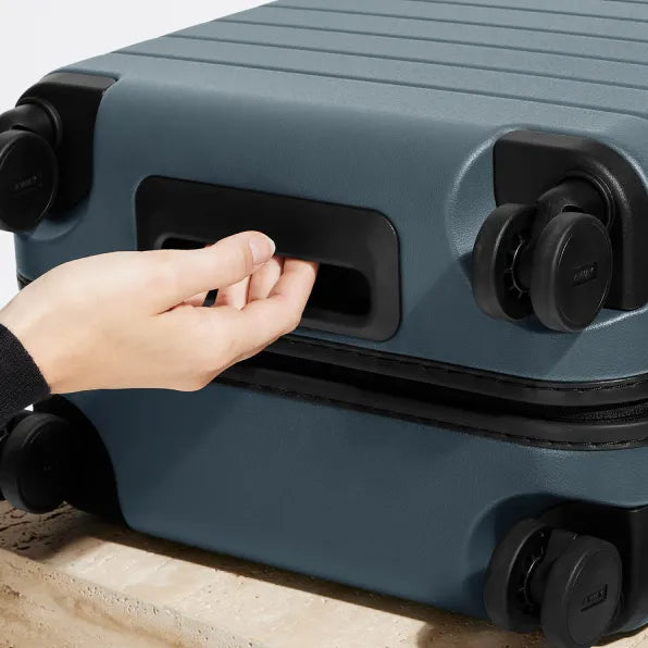 A close up shot of a woman holding the underside grab handle on an Away blue suitcase
