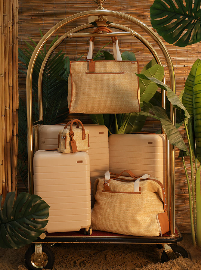 A set of Away x White Lotus luggage on a dolly surrounded by plants