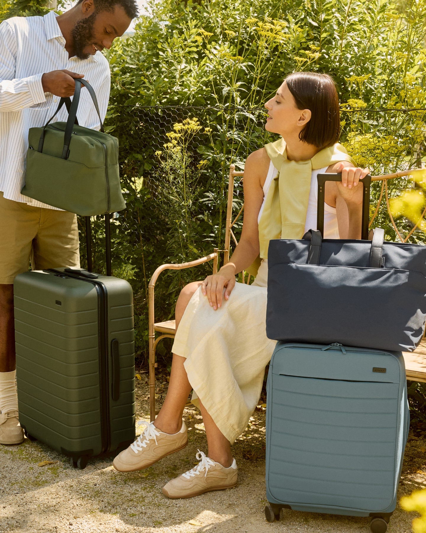 Two people sitting outside with an Away green luggage set and blue set