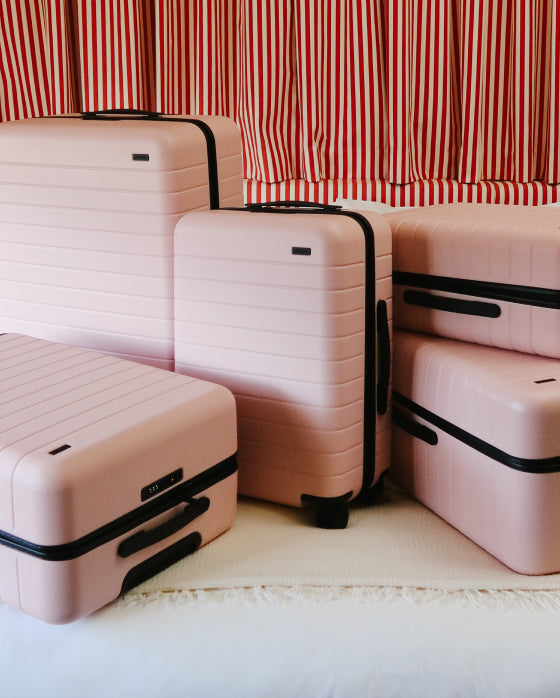 Set of pink suitcases with black handles against a red and white striped curtain background
