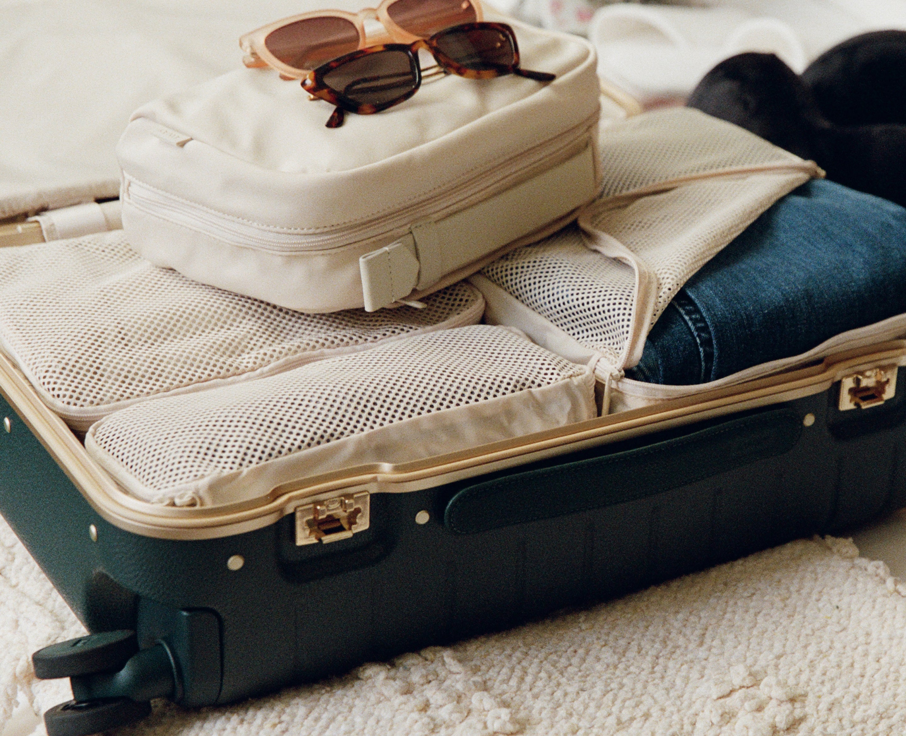 Open suitcase with clothes and a bag inside, on a bed.