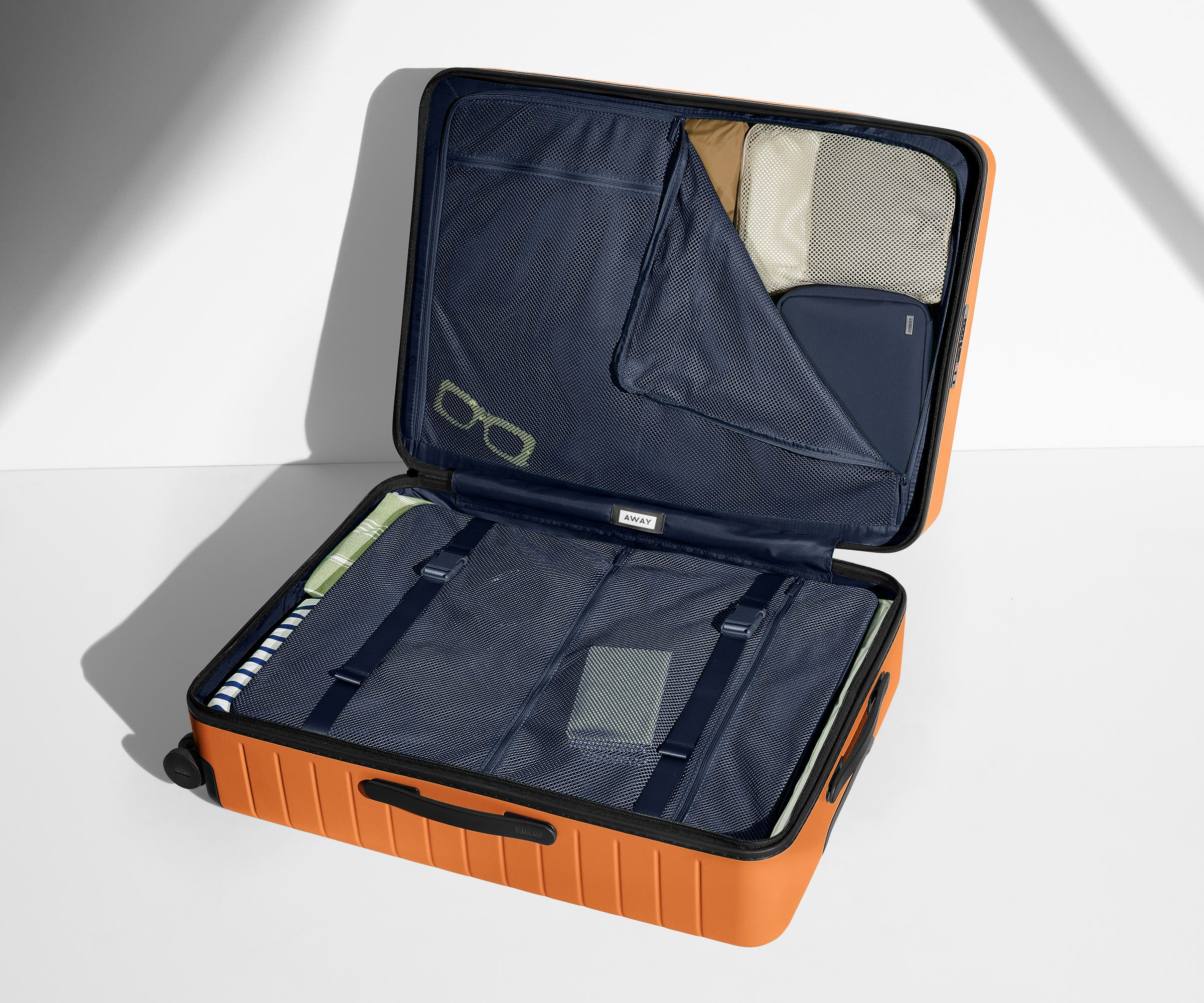 The Large suitcase in Sorbet Orange shown open on its side and packed with Away's packing organizers to show capacity and the interior compression system, designed to help you pack more in