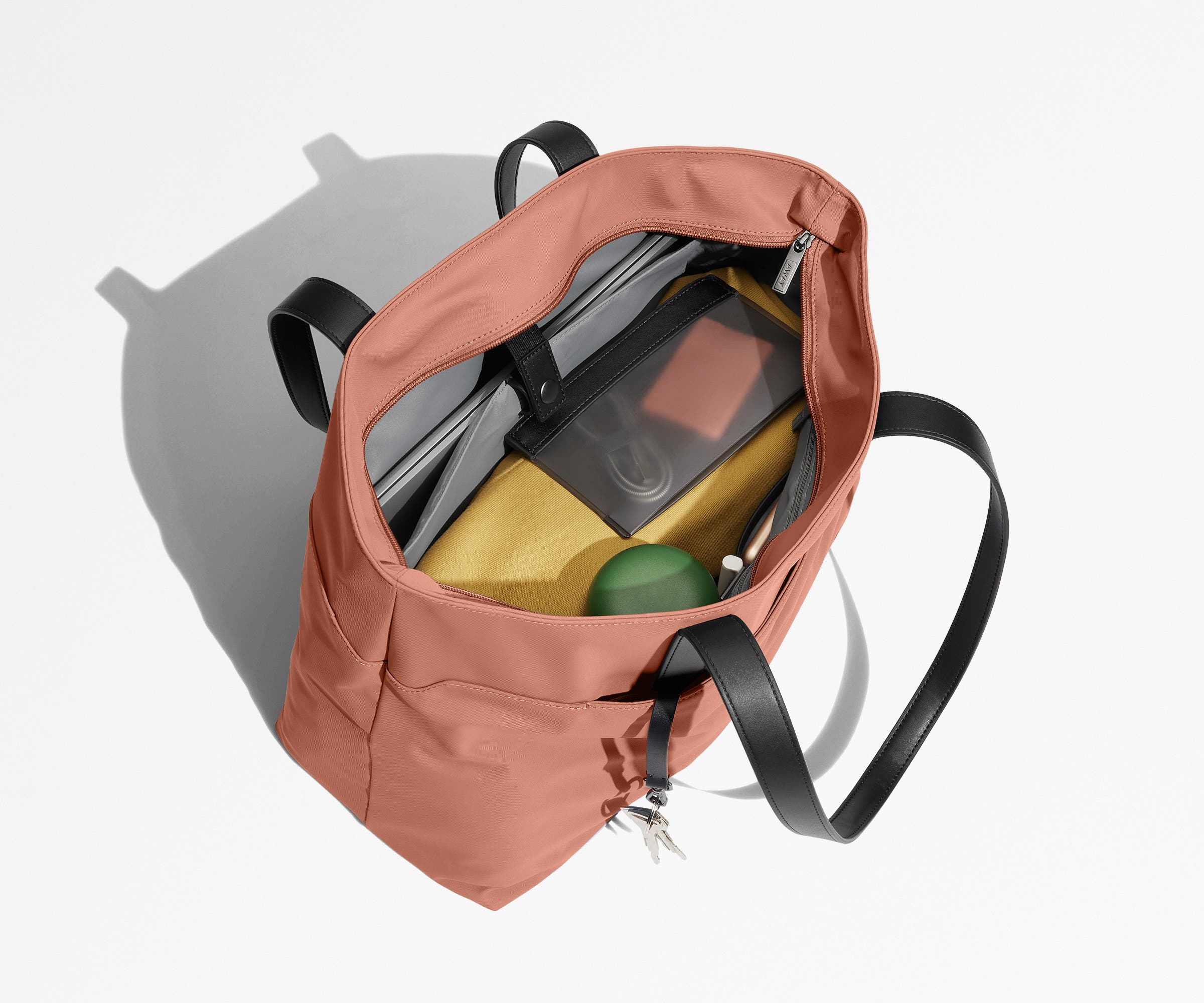 Tote bag packed with a laptop, water bottle, travel pouch, and sweater. A key is attached to the hidden key leash