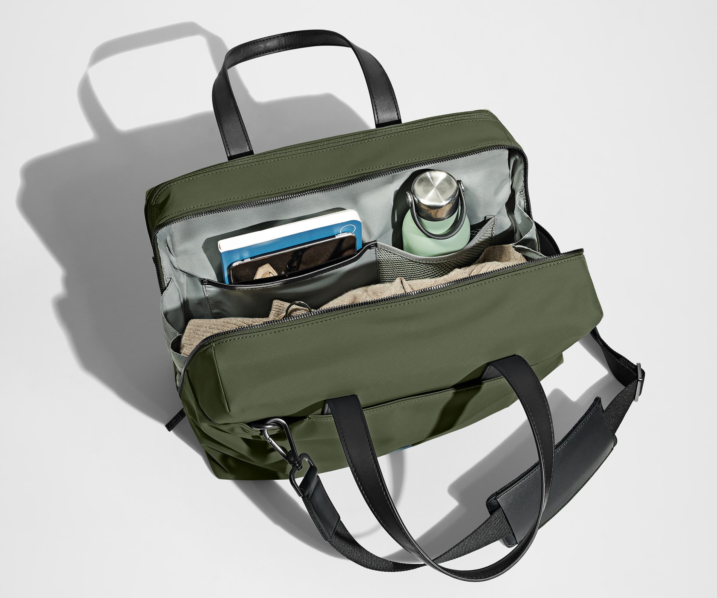 Main compartment packed with a light sweater, notebook, tablet, and water bottle. The detachable shoulder strap is clipped onto the bag.