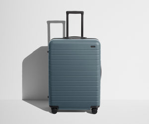 Front product view of The Medium suitcase in Coast Blue with raised handle
