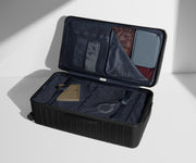 The Trunk suitcase in Jet Black shown open on its side and packed with Away's packing organizers to show capacity and the interior compression system, designed to help you pack more in