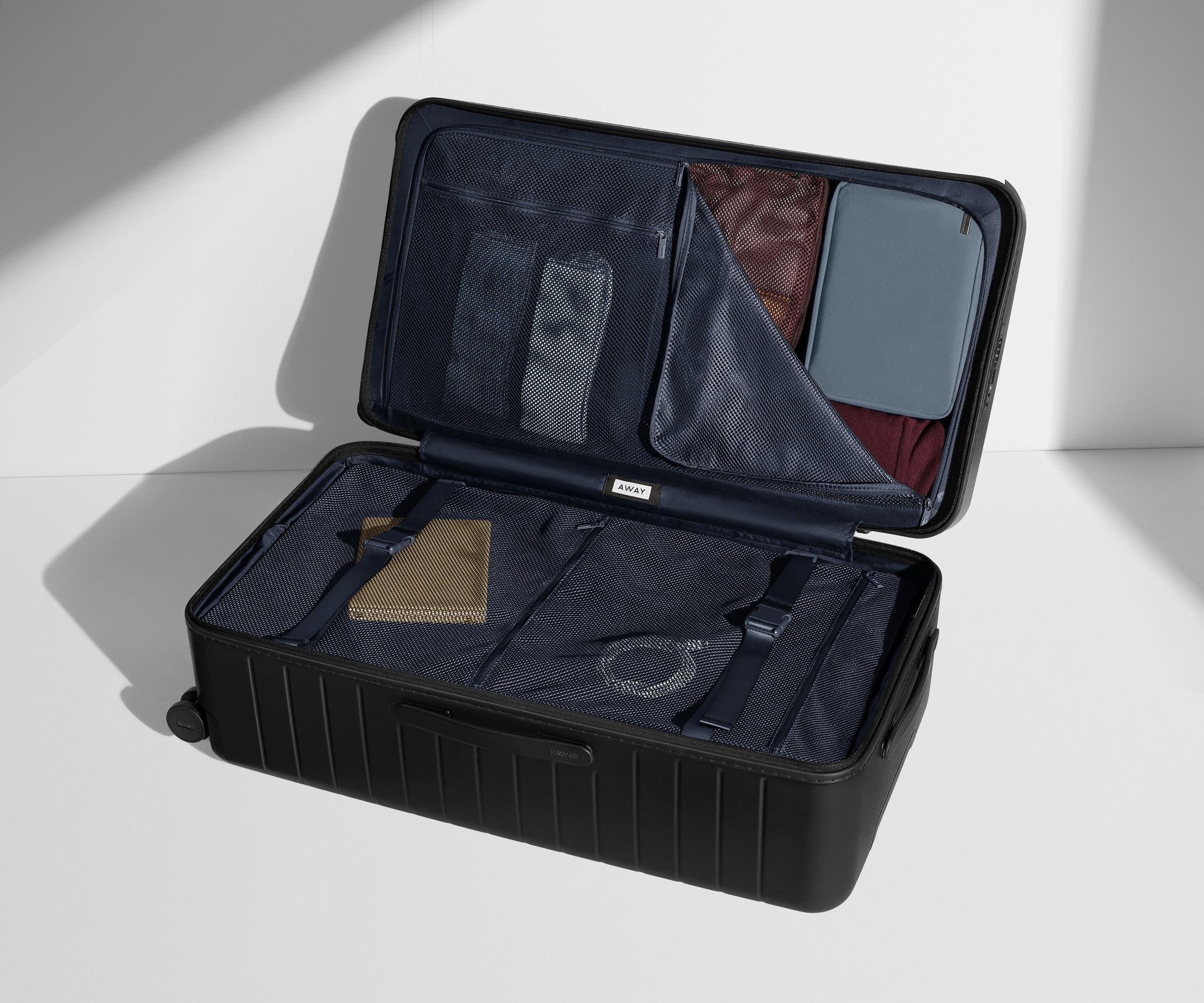 The Trunk suitcase in Jet Black shown open on its side and packed with Away's packing organizers to show capacity and the interior compression system, designed to help you pack more in