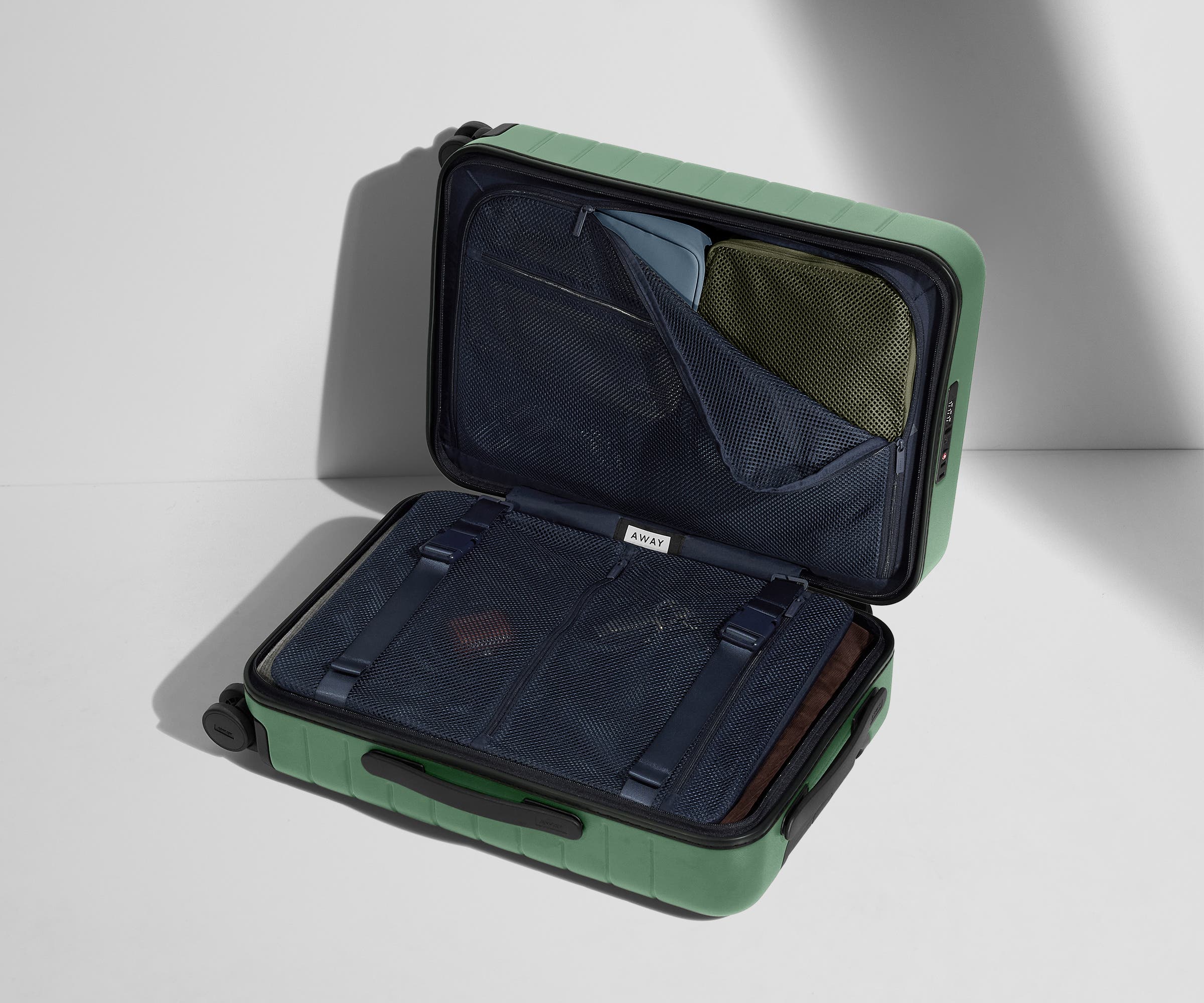 The Carry-On suitcase in Sea Green shown open on its side and packed with Away's packing organizers to show capacity and the interior compression system, designed to help you pack more in