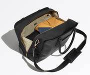 Leather duffle bag shown unzipped and packed with travel essentials, including clothing and a passport holder