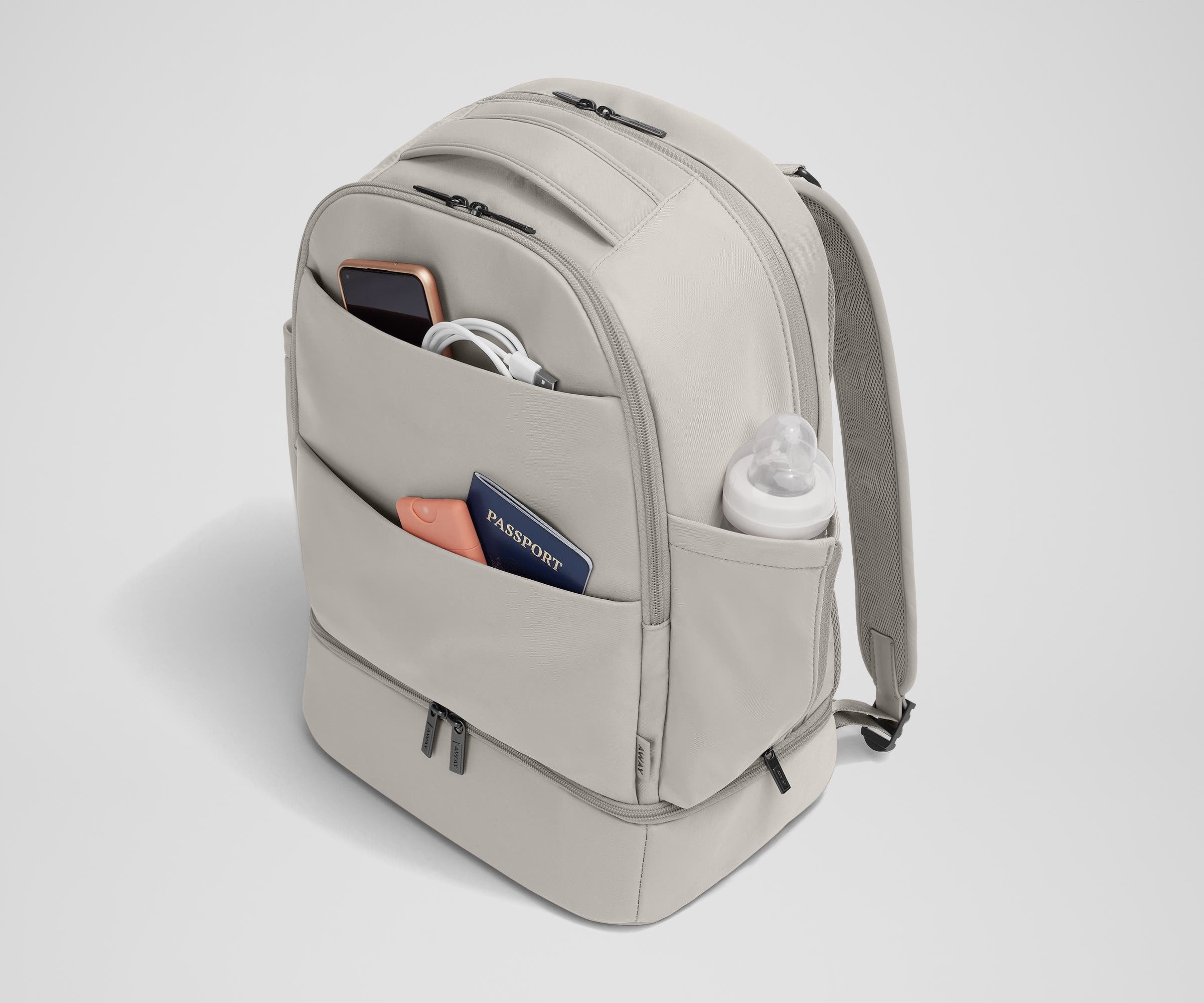 Exterior front pockets packed with travel essentials like a passport and phone, and the exterior bottle pocket packed with a milk bottle
