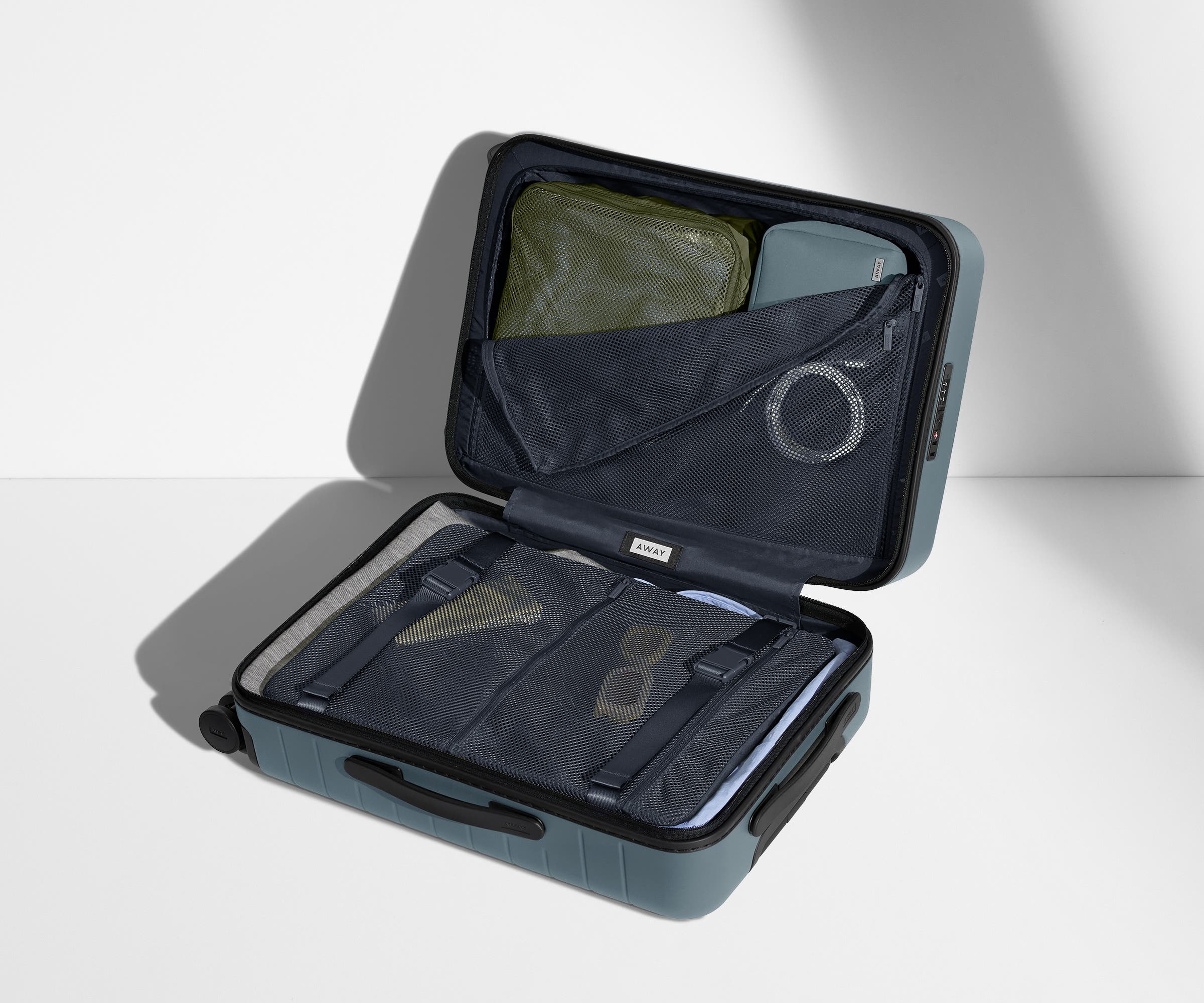 The Bigger Carry-On suitcase in Coast Blue shown open on its side and packed with Away's packing organizers to show capacity and the interior compression system, designed to help you pack more in
