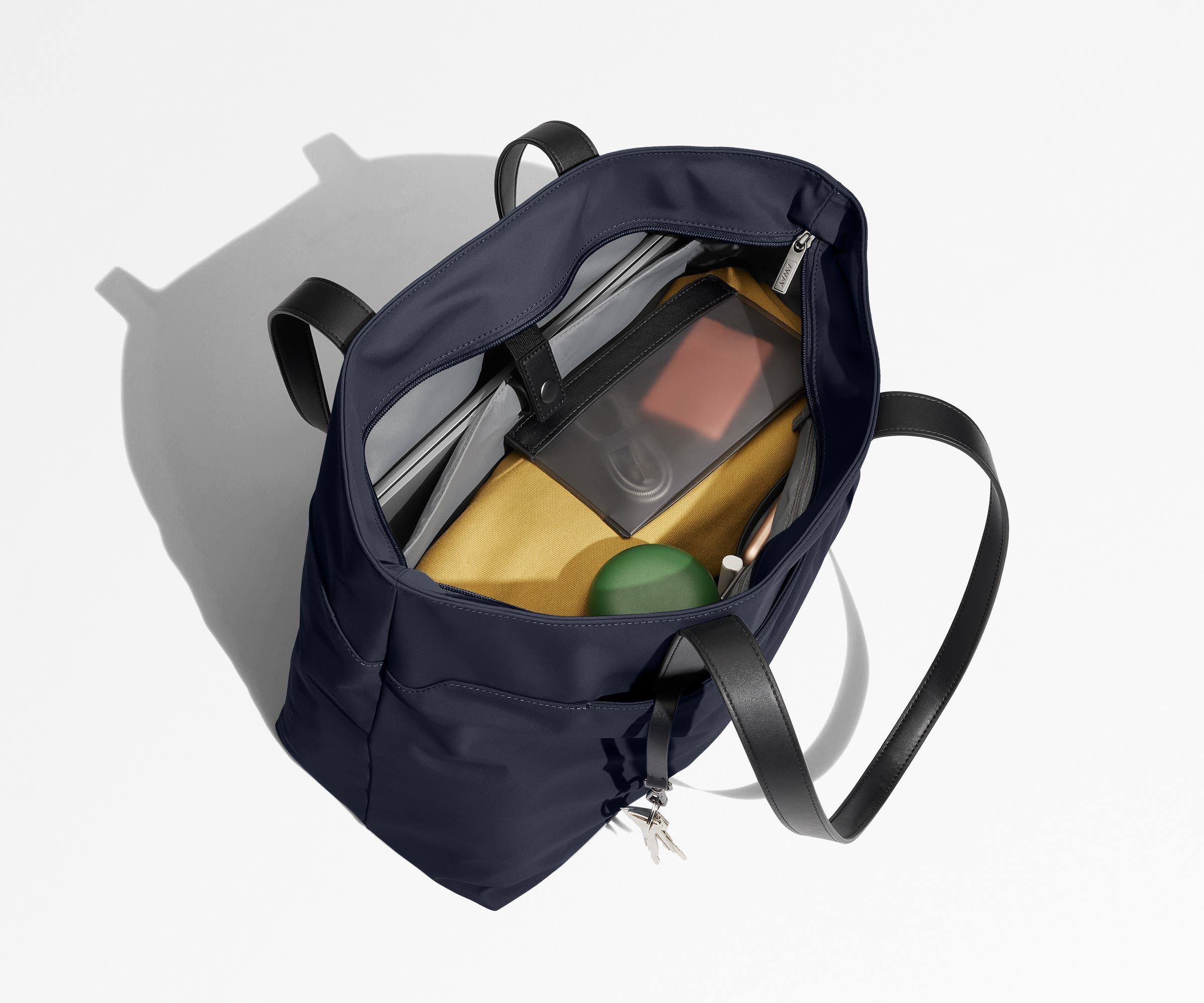 Tote bag packed with a laptop, water bottle, travel pouch, and sweater. A key is attached to the hidden key leash