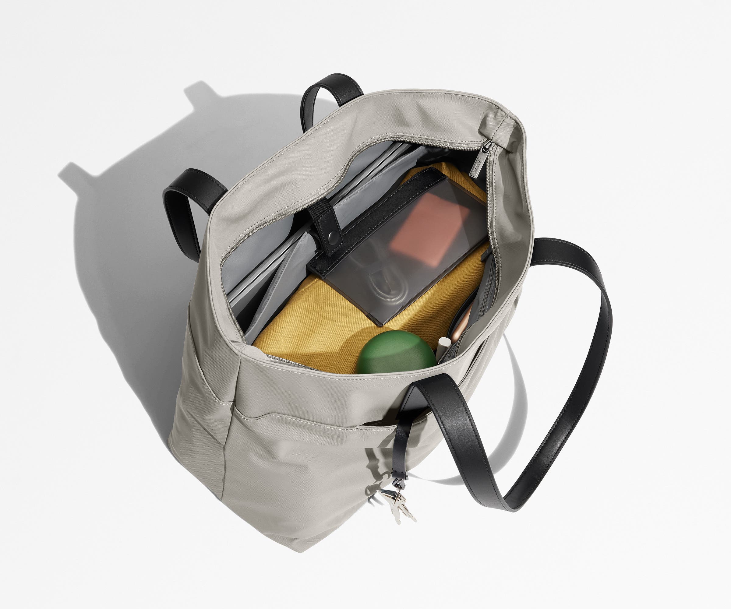 Tote bag packed with a laptop, water bottle, travel pouch, and sweater. A key is attached to the hidden key leash