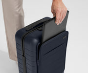 Zoomed in shot of talent slipping a laptop into the front pocket of The Front Pocket Carry-On in Navy Blue