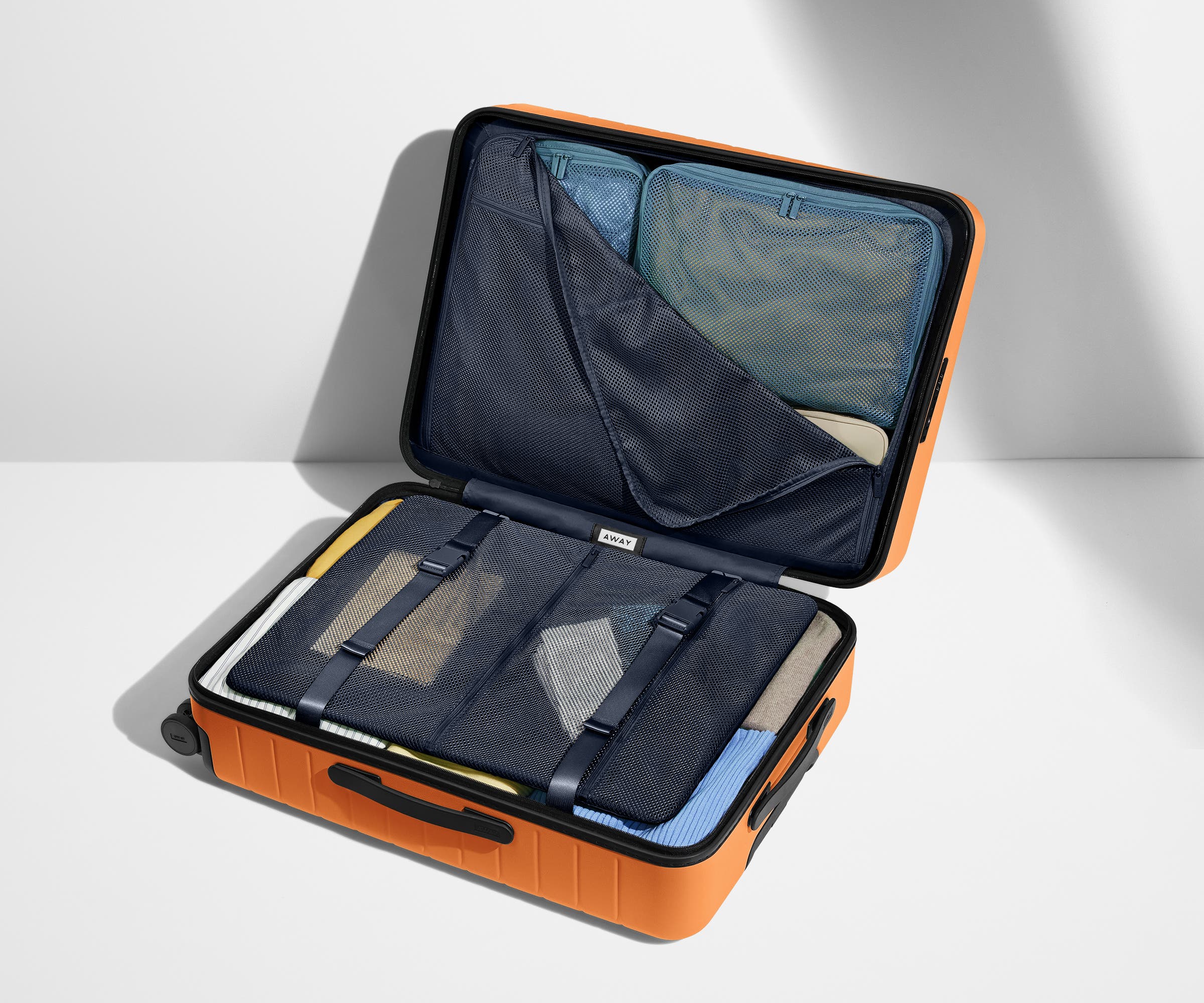 The Medium suitcase in Sorbet Orange shown open on its side and packed with Away's packing organizers to show capacity and the interior compression system, designed to help you pack more in