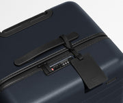 The Trunk suitcase in Navy Blue shown shown from above highlighting TSA-approved combination lock and recycled leather luggage tag