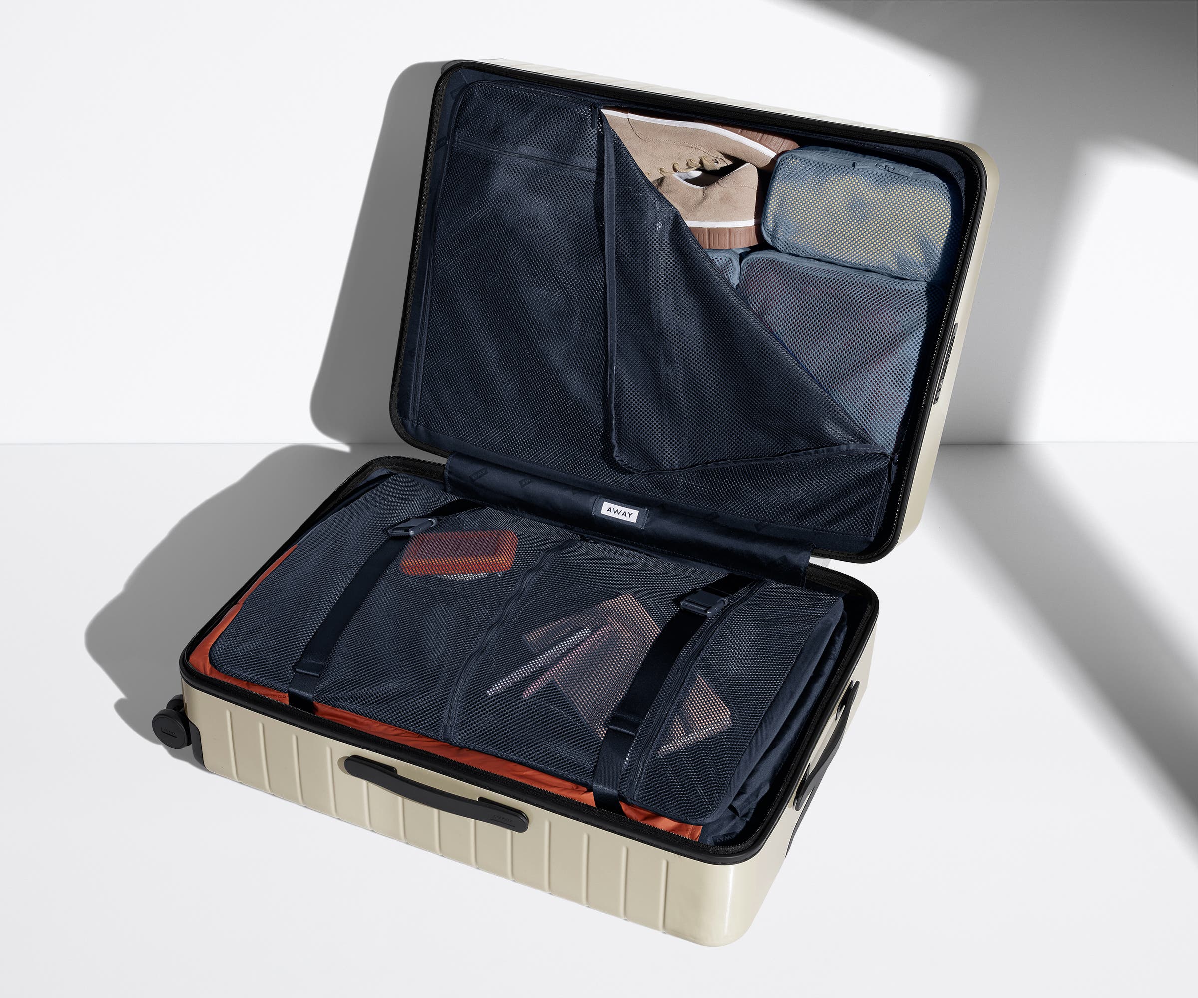 The Large suitcase in Salt White (Gloss) shown open on its side and packed with Away's packing organizers to show capacity and the interior compression system, designed to help you pack more in