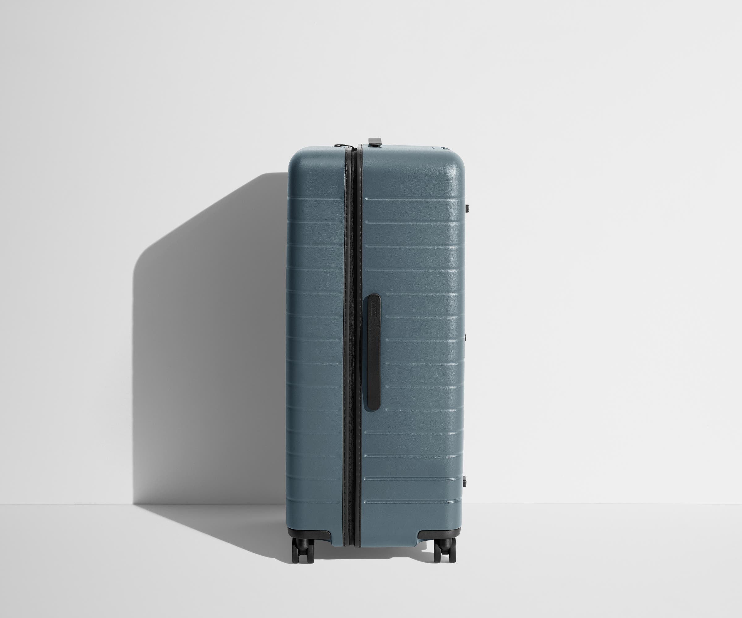 Side product view of The Trunk suitcase in Coast Blue to show the slimmer top lid and deeper main compartment for easy access and packing