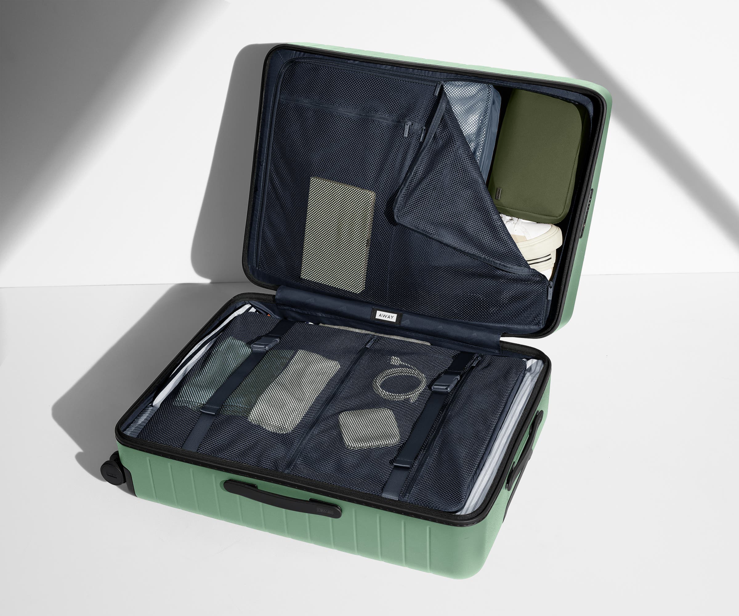 The Large suitcase in Sea Green shown open on its side and packed with Away's packing organizers to show capacity and the interior compression system, designed to help you pack more in