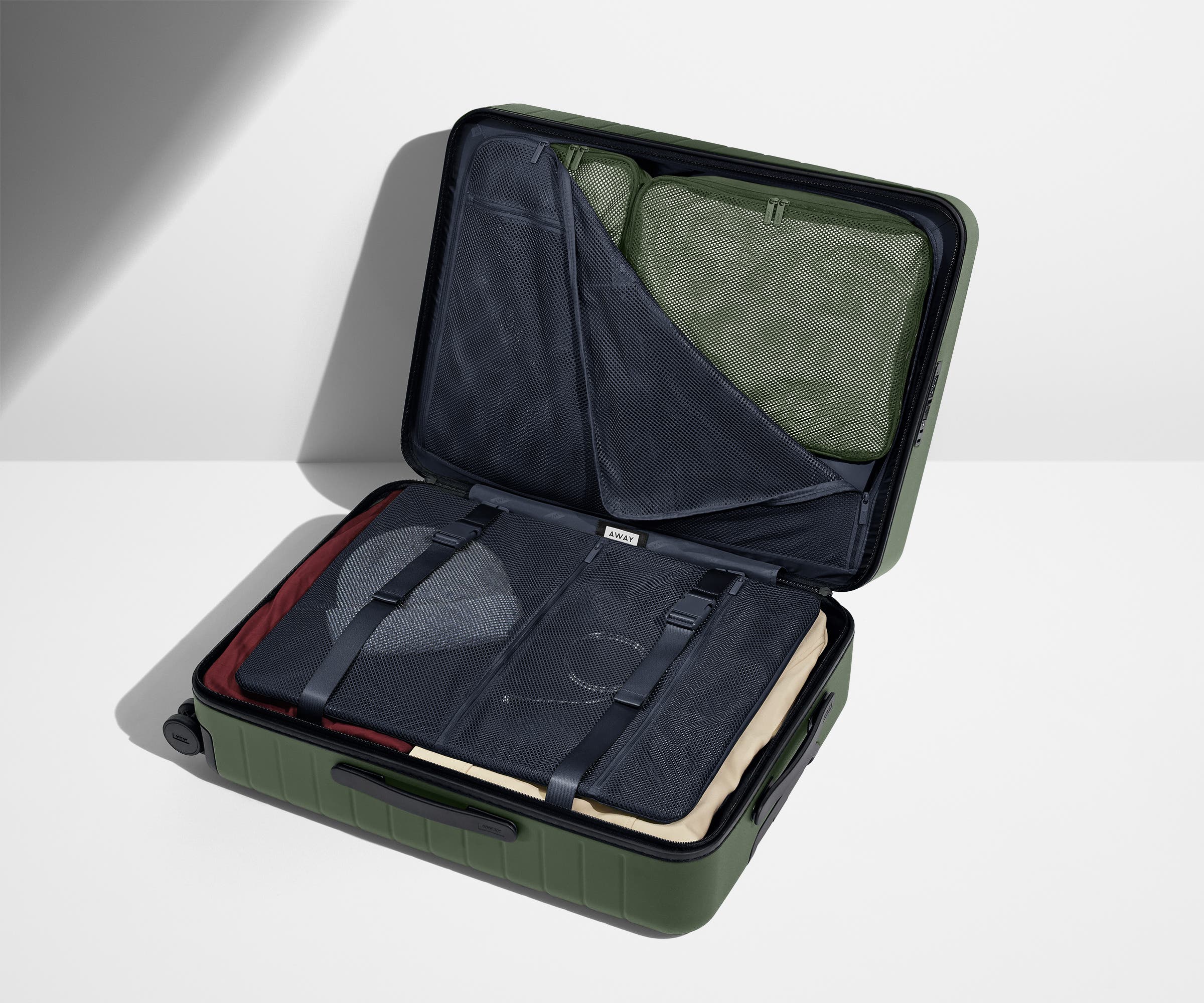 The Medium suitcase in Olive Green shown open on its side and packed with Away's packing organizers to show capacity and the interior compression system, designed to help you pack more in