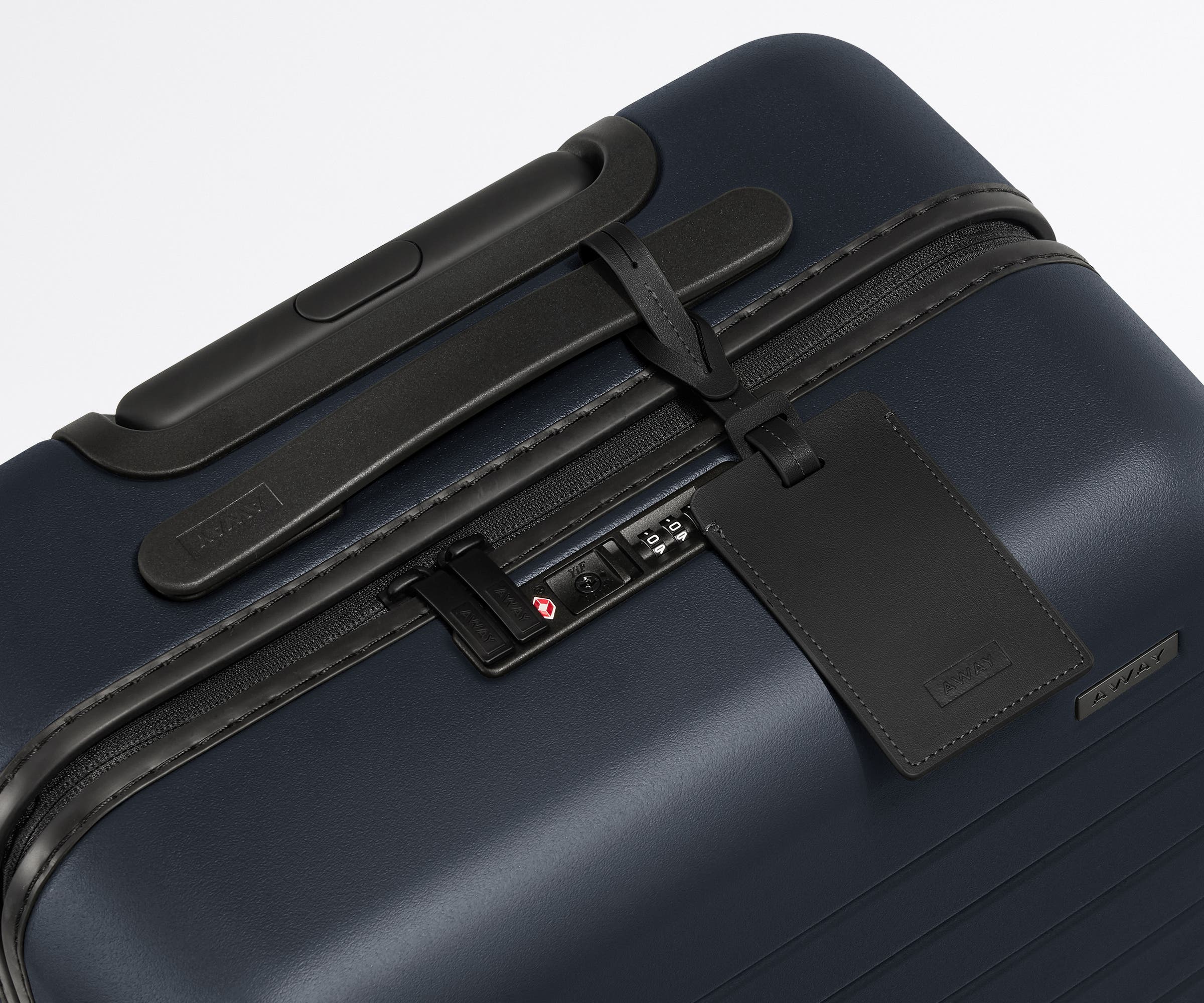 The Carry-On suitcase in Navy Blue shown shown from above highlighting TSA-approved combination lock and recycled leather luggage tag