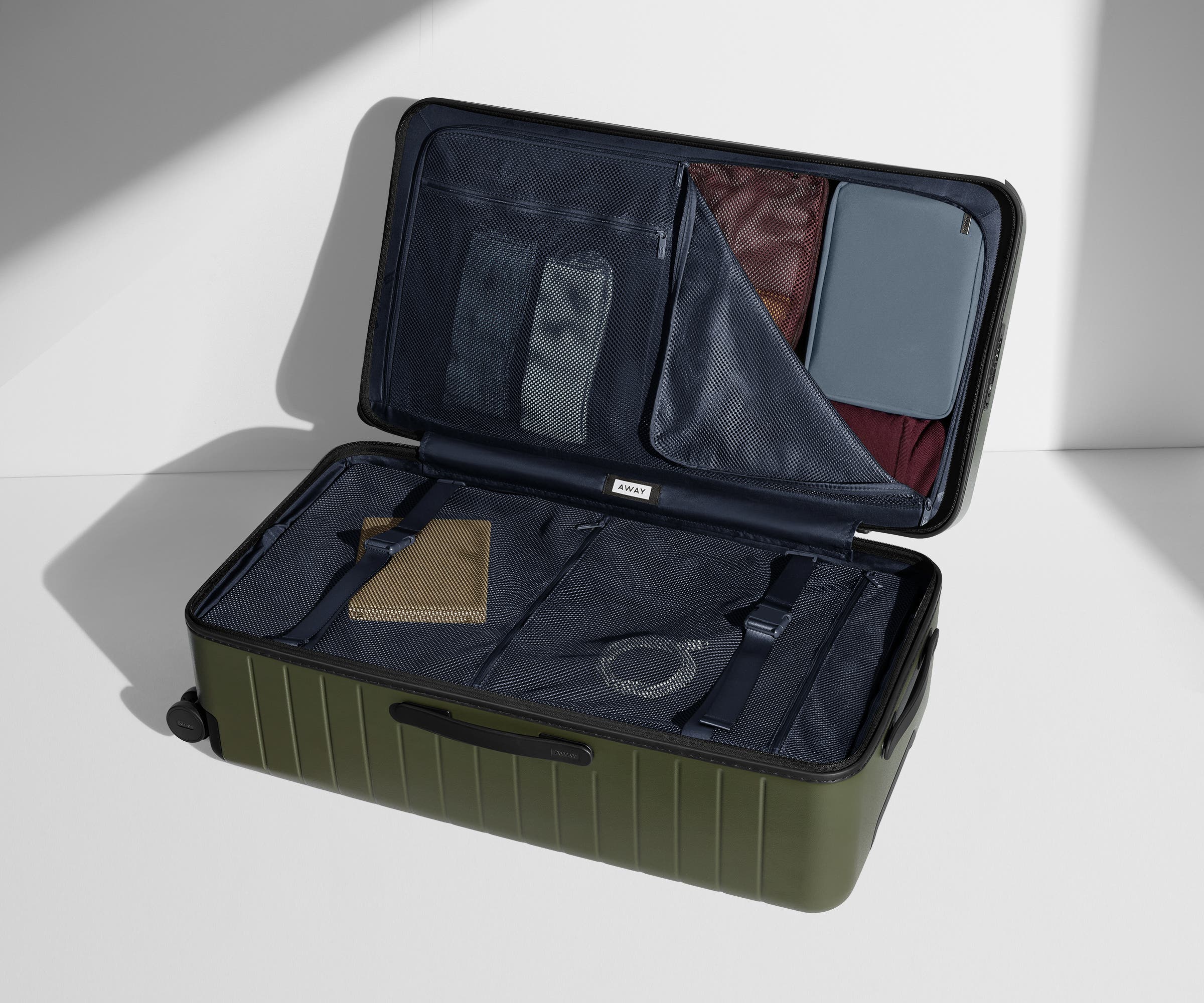 The Trunk suitcase in Olive Green shown open on its side and packed with Away's packing organizers to show capacity and the interior compression system, designed to help you pack more in