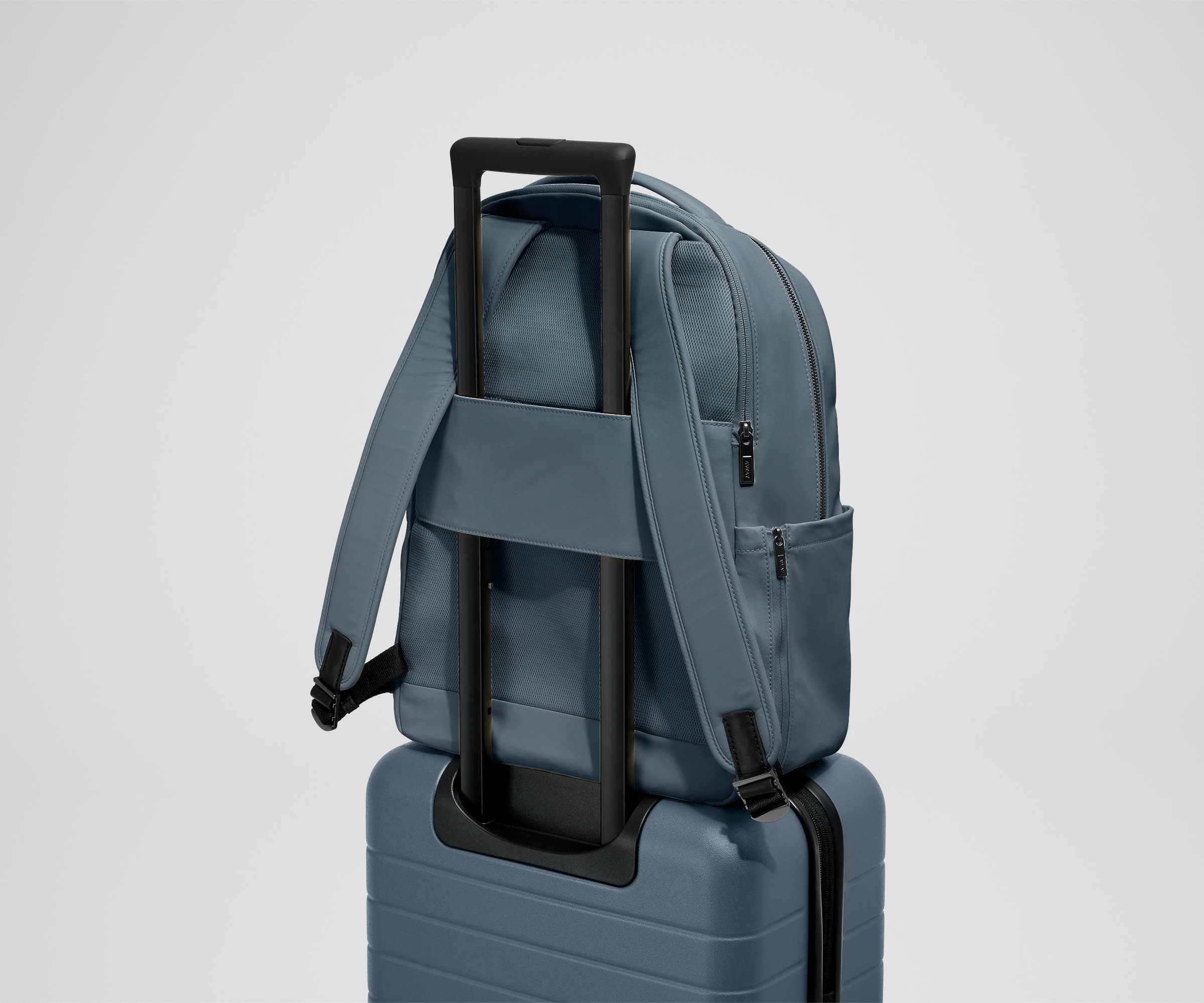 The Commuter Backpack on top of an Away suitcase, attached by the trolley pass-through sleeve