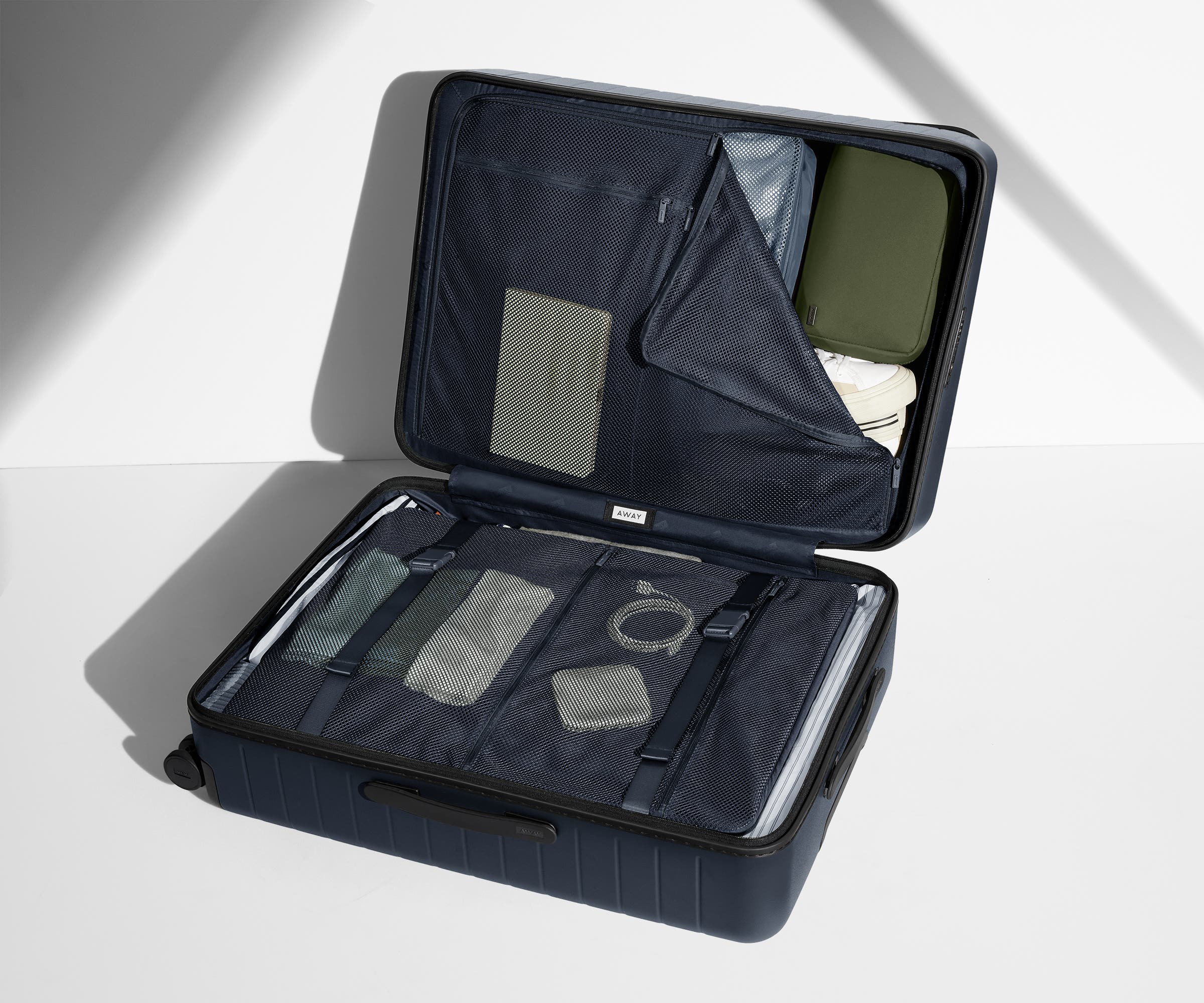 The Medium suitcase in Navy Blue shown open on its side and packed with Away's packing organizers to show capacity and the interior compression system, designed to help you pack more in