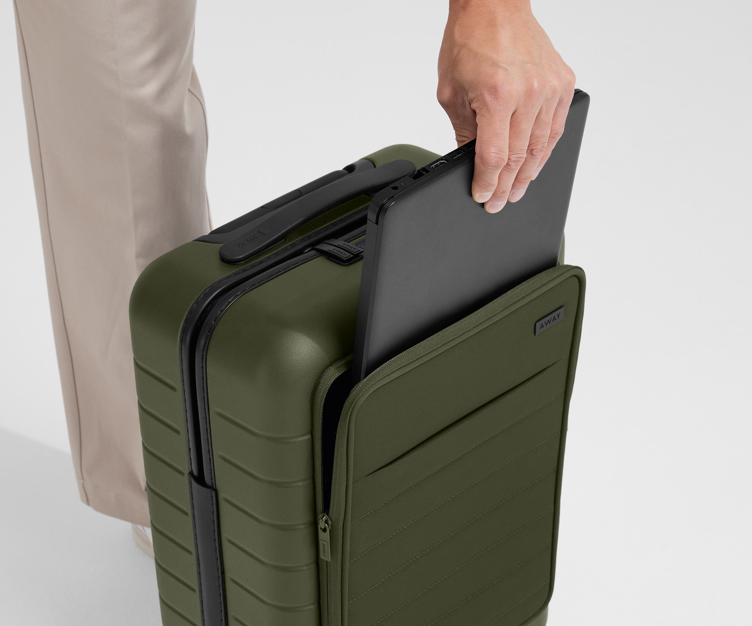 Zoomed in shot of talent slipping a laptop into the front pocket of The Front Pocket Carry-On in Olive Green