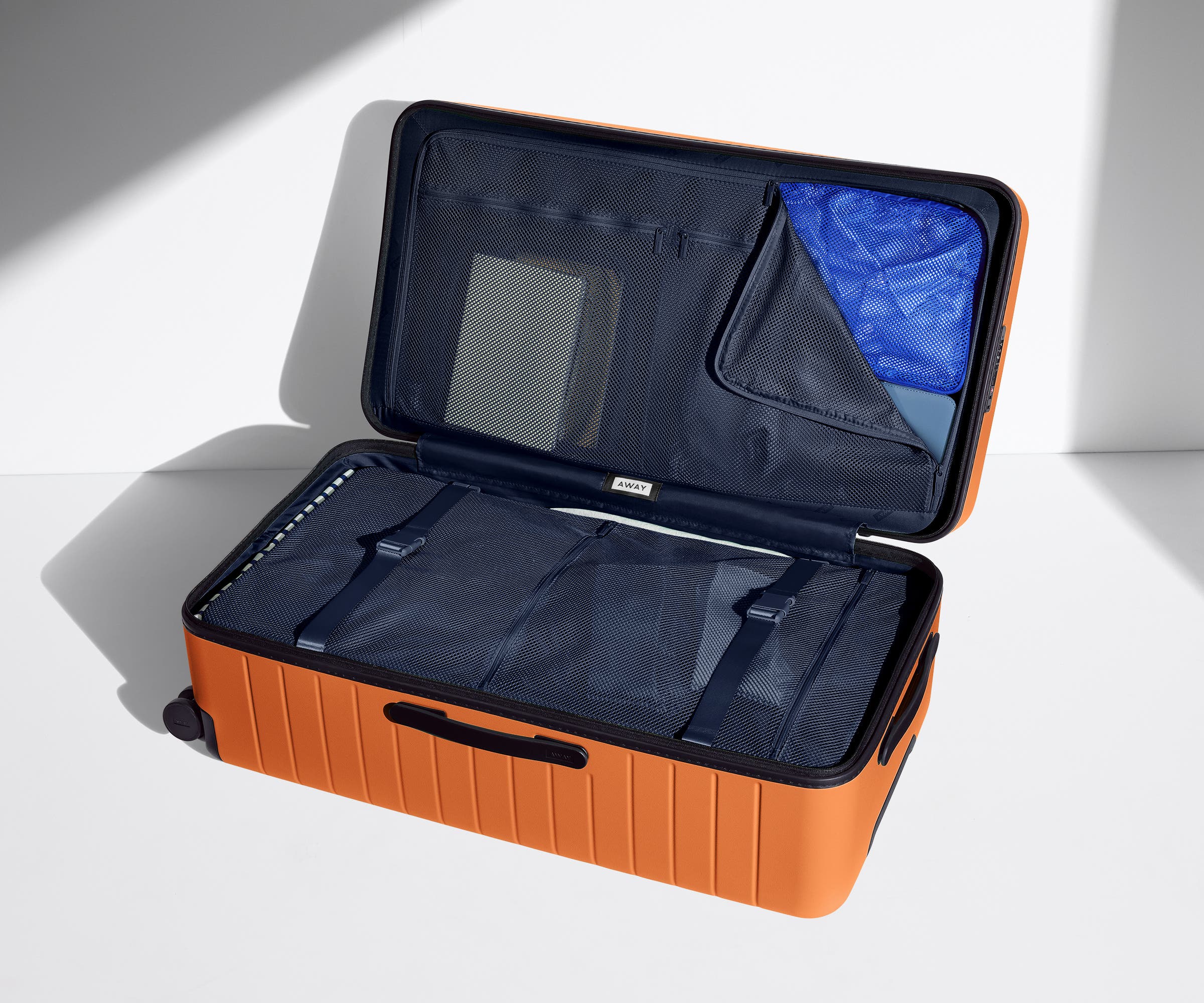 The Trunk suitcase in Sorbet Orange shown open on its side and packed with Away's packing organizers to show capacity and the interior compression system, designed to help you pack more in